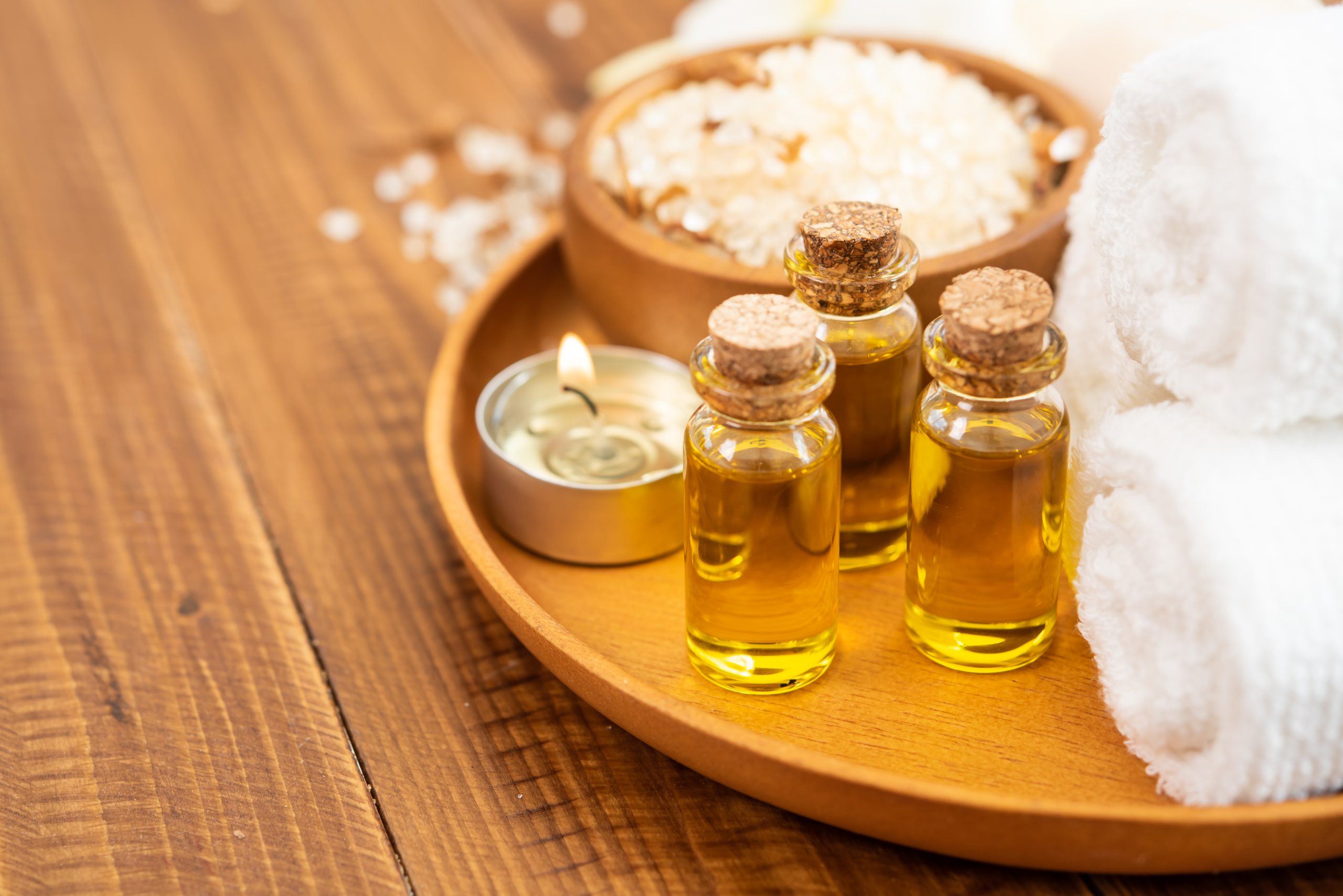 Sea salt, towels, aroma oil in bottles and flowers on vintage wooden background. Selective focus.